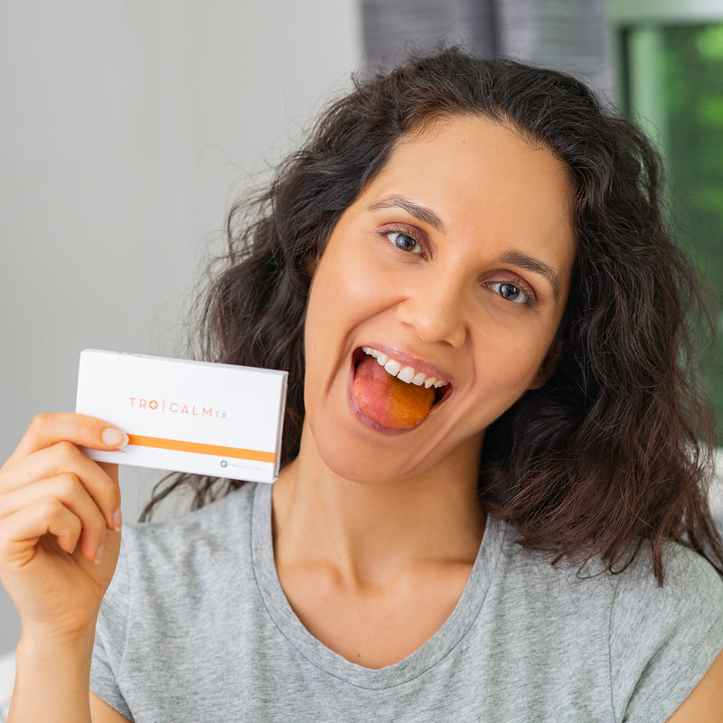 Woman with orange tongue from Tro Calm while holding a box of Tro Calm